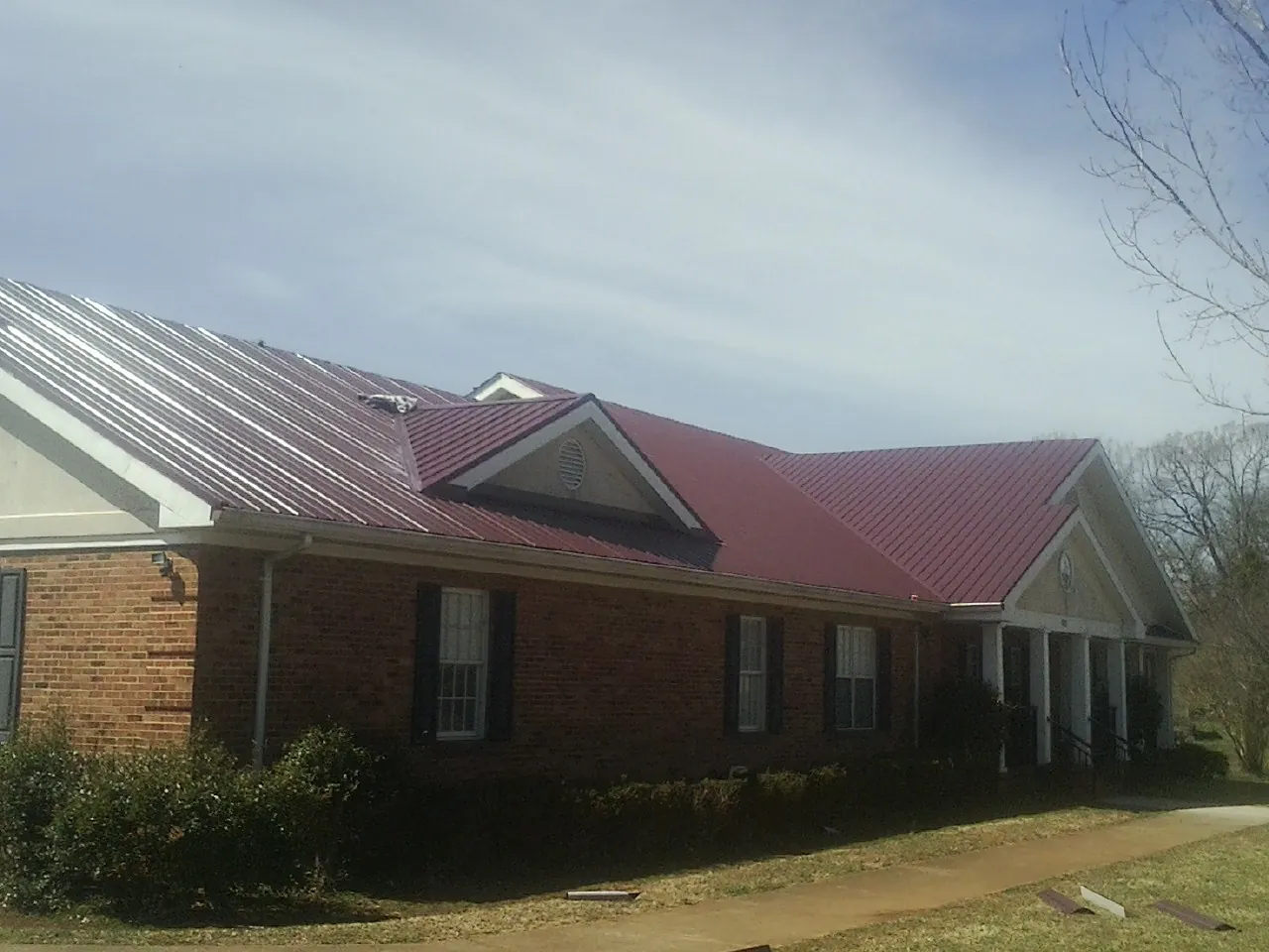 Red metal roof with gabled entries on a long brick building, from a Hail Damage Roof Repair job in Brielle