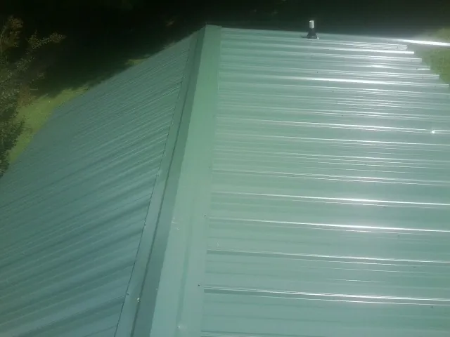 New green metal panels meeting at the ridge of a roof — Flat Roof Repair work by our crew in Brielle