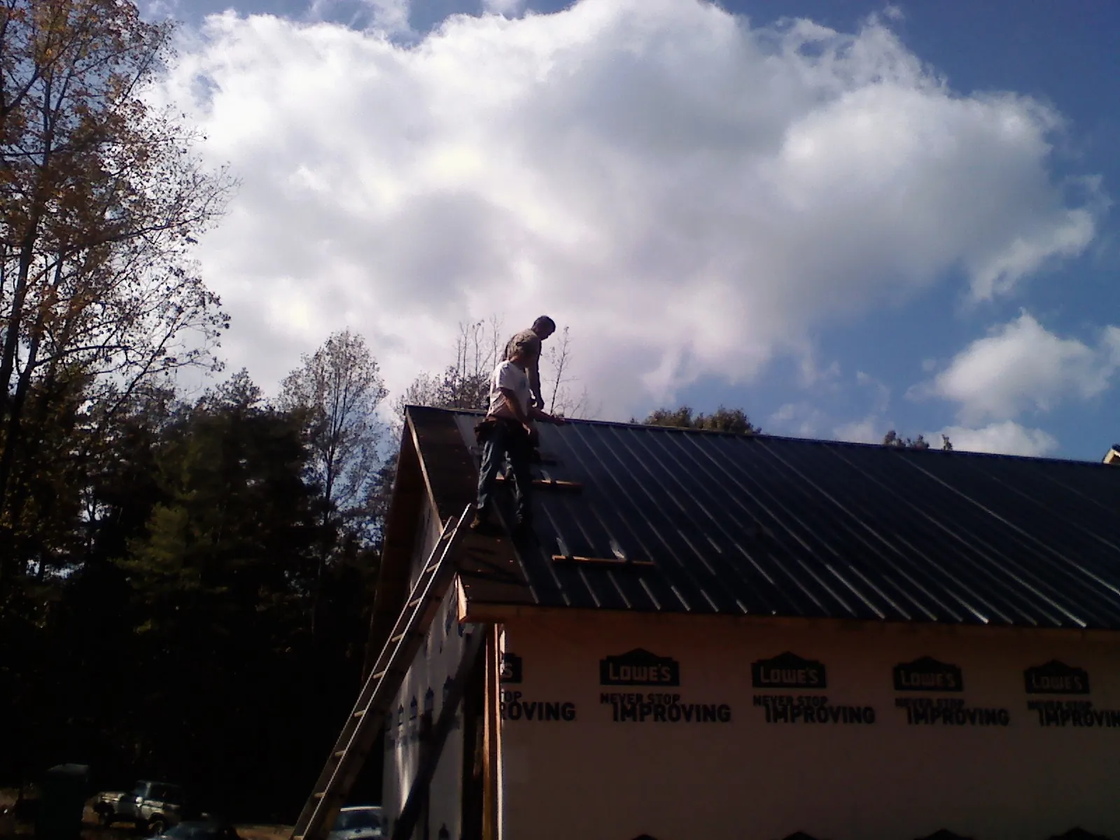 Roofer fastening dark metal panels high against a cloudy sky, from a Roof Inspection job in Brielle